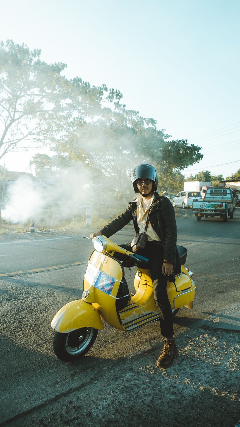 A young man enjoying a sunny ride on a yellow Vespa in East Java, Indonesia.