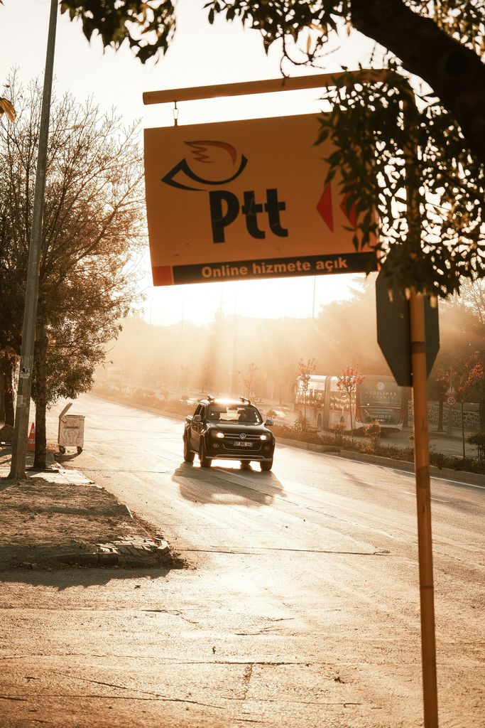 Silhouetted street scene at sunset with a Ptt sign and car driving.
