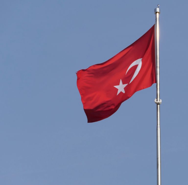 Turkish national flag waving against a clear blue sky, symbolizing national pride.